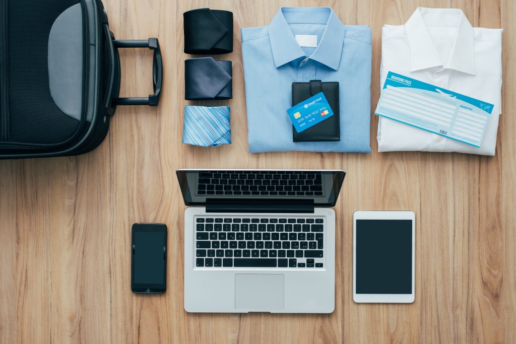 Planning a business trip: bag, formal clothing, credit cards and plane tickets on a desk with laptop, smartphone and tablet, traveling and technology